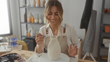 Kadın seramik stüdyosunda çömlek çarkına seramik vazo boyuyor; yaratıcılık odaklı sükunet.