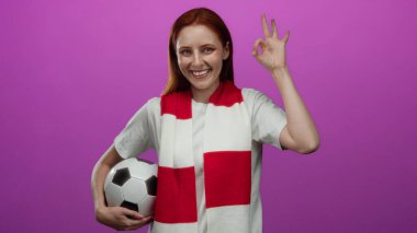 Futbol topu takan kadın pembe arka planda onay işareti gösteriyor, destek ve mutluluk gösteriyor..