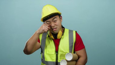 Kasketli ve yelekli genç adam inşaat bağlamında mizah taşıyan beyaz bir geçmişe karşı alaycı bir ağlama hareketi yapıyor..