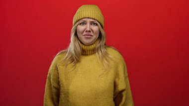 Sarı süveter ve bereyle gülümseyen bir kadın canlı kırmızı bir arka planda basit bir stille sıcaklık ve neşe saçıyor..