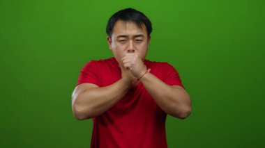 Kırmızı gömlekli, yeşil arka planda boğazı ağrıyan genç adam rahatsız ve ağrılı görünüyor, boynunu sıkıyor sanki rahatsızlık ya da acı çekiyormuş gibi..