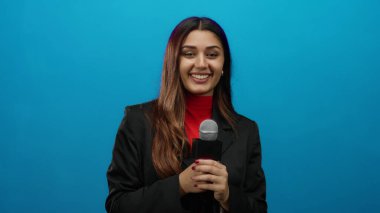 İspanyol kadın muhabir canlı mavi bir arka plana karşı elinde bir mikrofon tutarken özgüvenle gülümsüyor, yayıncılıktaki profesyonellik ve coşkuyu somutlaştırıyor..