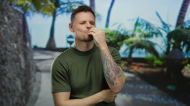 Sokak ortasında gülümseyen bir adam dövmeleri ve ağaçları olan canlı yeşillik ve günlük kıyafetlerle keyif ve memnuniyet veren bir adam..