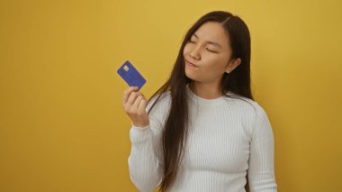 Kadının kredi kartını izole edilmiş sarı arka planda tutarak düşünceli ifade ve modern yaşam tarzı kavramını aktarıyor..