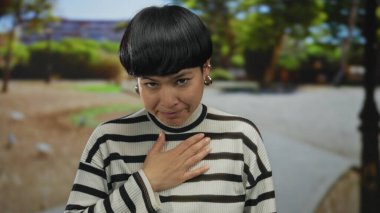 Çizgili kazaklı bir kadın açık havada canlı yeşil bir park ortamında şükranlarını sunarak huzurlu ve huzurlu bir anı yakalıyor..