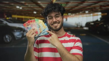 Kapalı alanda gülümseyen bir adam loş bir park alanında İsviçre frangı tutuyor, modern şehir yaşam tarzını ve finansal başarısını vurguluyor..