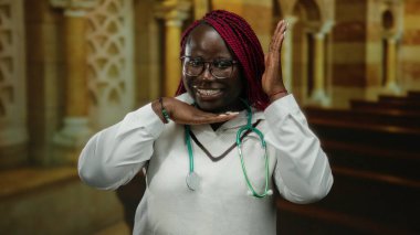 Steteskoplu kendinden emin bir kadın kilise ortamında gülümsüyor, elleriyle çerçeve hareketi yapıyor, gözlük takıyor, sağlık ve maneviyat bağlantısını tasvir ediyor..