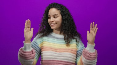 Kıvırcık saçlı, elleri mor arkaplan üzerinde hareketli pastel renkli gökkuşağı süveter giyen kadın.