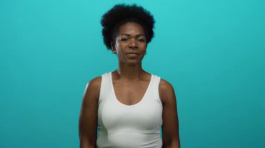 İzole edilmiş mavi arka planda güvenle gülümseyen bir kadın olumlu ve mutluluk saçan bir başparmak verir..