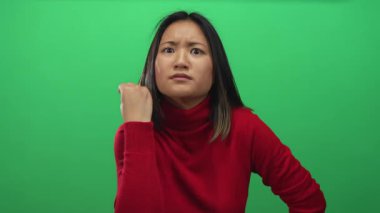 Kırmızı kazaklı genç bir kadın, yeşil bir arka plan duvarına karşı elleri ile anlamlı bir jest yapıyor. Duygularını ve dikkatini ifade ediyor..