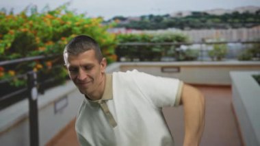 Açık bir gökyüzünün altında yemyeşil bir yeşil ile çevrili canlı bir sokakta gülümseyen bir adam..