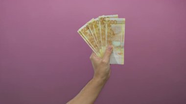 Filipin pesolarını canlı pembe arka planda tutan beyaz bir adamın eli..