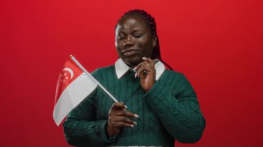 İzole edilmiş kırmızı arka planda Singapur bayrağı tutan bir kadın. Kendine güvenen ve gururlu görünen yeşil kazak giyen bir kadın..