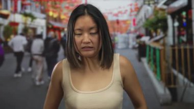 Düşünceli bir ifadeye sahip genç bir kadın hareketli bir şehir caddesinde yürüyor, etrafı renkli dekorasyonlarla çevrili, gelenek ve şehir canlılığının bir karışımını sergiliyor..