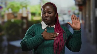 Şehir terasında söz veren bir kadın yeşil bir kazak giyiyor, örgülü saçlarıyla, canlı bir açık hava restoranında samimiyet ve bağlılık gösteriyor..