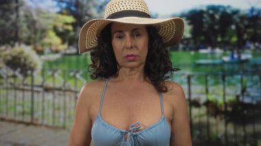 Bikinili ve şapkalı İspanyol kadın yemyeşil bir parkta güneşli bir günün tadını çıkarıyor. Çevresi gür doğa ve ağaçlarla çevrili..