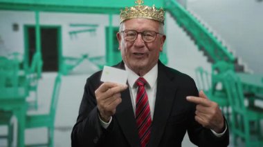 Açık hava restoranının terasında taç tutan kıdemli bir adam neşe içinde gülüyor, bir iş ortamında başarı ve kutlama sunuyor..