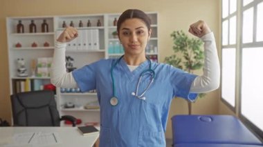 İspanyol kadın doktor bir hastane odasında kollarını rahatça esnetiyor, tıbbi bir iş yerinde güç ve profesyonellik gösteriyor..