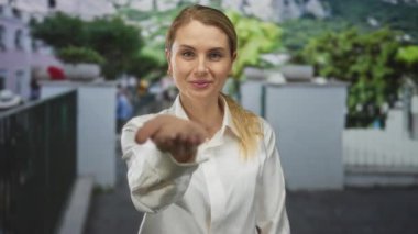 Şehir sokaklarında elini uzatan, şehir geçmişi ve yeşilliği bulanık beyaz tişörtlü bir kadın. Etkileşim ve iletişim sergiliyor..