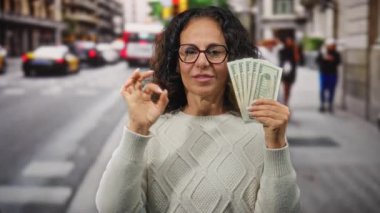 Şehirdeki kadın, bize dolar tutarken, güven ve finansal başarıyı gösterirken, el hareketleriyle sorun çıkarmıyor..