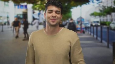 Erkek adam kollarını kaldırır ve onları caddenin karşısına dağıtır. Genç İspanyol adam dışarıda durup neşeyle gülümserken..