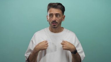 Stüdyoda nane yeşili arka planda çıplak kollarıyla göğsünü gösteren Latin asıllı genç bir adam sürpriz kimlik..