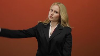 Kendine güvenen bir pozla kolunu uzatan kadın, güçlü, kendine güvenen ve kadınsı bir görünüm sergiliyor, profesyonel bir bağlamda gücünü gösteriyor..