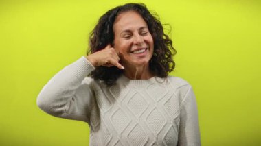 Kıvırcık saçlı, neşeli sarı bir arka planda telefonla konuşuyormuş gibi gülümseyen ve jestler yapan olgun İspanyol kadın sıcaklığı ve iletişimi yayıyor..