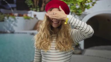 Havuz kenarını kapatan kadın gözleri, genç sarışın el bereyi kilitliyor ve çizgili üst kısmı çerçeveliyor..