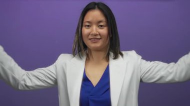 Beyaz ceketli, mavi gömlekli, mor duvarın karşısında duran, gülümseyen bir kadın..