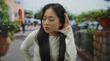 Sokak ortasında meraklı bir ifadeyle dinleyen bir kadın yeşillik sırasına dizilmiş genç Çinli kadınların samimi görüntülerini yakalıyor..