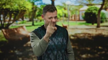 Genç adam parkın dışındaki canlı ağaçlar ve bankların olduğu bir yerde neşeli ve pozitif bir atmosferi yakalayarak gülümsüyor..