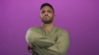 Neşeli pembe arka plana karşı ciddi ifadeleri olan genç İspanyol bir adam sıradan süveter kollarıyla kararlılık ve başkaldırı içinde çapraz