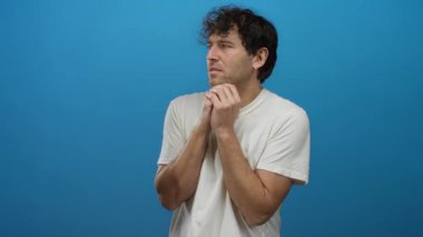 Endişeli ifadeye sahip İspanyol bir adam, basit bir beyaz gömlek giymiş, mavi bir arka plana gergin bir şekilde el sıkışıyor..