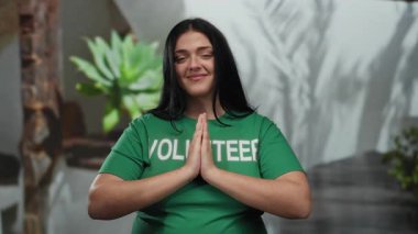 Şehir merkezinde yeşil gönüllü gömleği içinde gülümseyen kadın çevresi yeşillik, somut pozitiflik ve toplum ruhuyla çevrili..