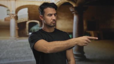 Siyah tişörtlü genç adam eski kasaba caddesinde duruyor. Açık hava kemerlerinin altında kendine güvenen bir ifadeyle ileri bakıyor..