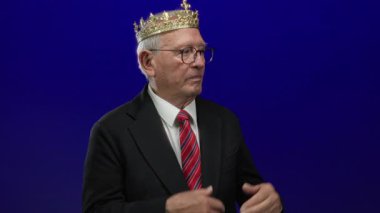 Takım elbiseli kıdemli bir adam, soyutlanmış mavi bir geçmişe karşı özgüvenli bir şekilde el kol hareketi yapar. Liderlik ve zarafeti kraliyet dokunuşu ve modern iş becerisiyle iletir..