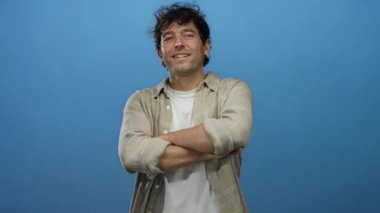 Kolları mavi bir zeminde çapraz gülümseyen bir adam, kendinden emin, gevşek İspanyol erkek davranışının altını çiziyor..