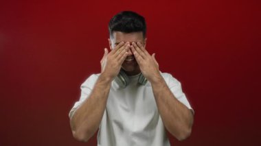 Yüzüne kulaklık takan, neşeli kırmızı arka plana gülen, mutluluk ve duyguyu ifade eden genç bir adam..