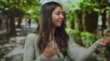 Genç İspanyol kadın, güneş ışığı altında yapraklı yeşil orman yolu boyunca elleri ile gitar jesti çalıyor..