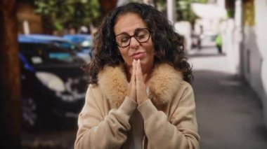 Kıvırcık saçlı, gözlüklü bir kadın sonbaharda şehir sokaklarında dua ediyor..