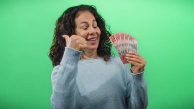 Avustralya banknotları tutan bir kadın yeşil izole bir duvara karşı olumlu bir jest, orta yaşlı güven ve finansal başarı sergiliyor.