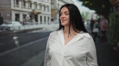 Beyaz gömlekli kadın şehir sokaklarında el kol hareketi yapıyor. İfadesini ve sohbetini şehir ortamında yansıtıyor..