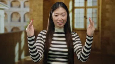 Çin 'de tarihi bir üniversite avlusunda el kol hareketi yapan, çizgili gömlek giyen, uzun saçlı, genç ve güzel, Asya kültürünü gözler önüne seren bir kadın..