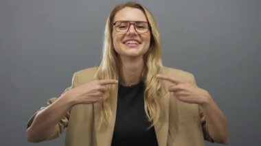 Gri arka planda, bej bir ceketle gülümseyen ve el kol hareketi yapan bir kadın..