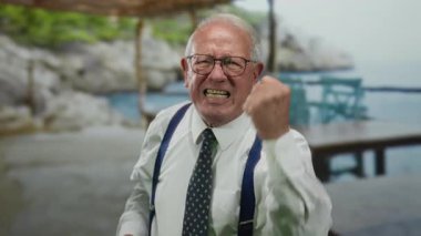 Takım elbiseli kıdemli işadamı, deniz kenarındaki bir sahilde yumruklarını sıkarak, açık hava ortamında yaşadığı hayal kırıklığını vurguluyor..