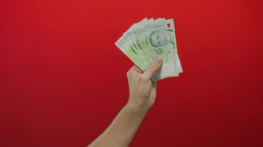 Dolarları canlı kırmızı bir duvara karşı tutan, kendinden emin bir şekilde para dağılımını gösteren, zenginlik ve finansal işlemler kavramını vurgulayan bir adam..