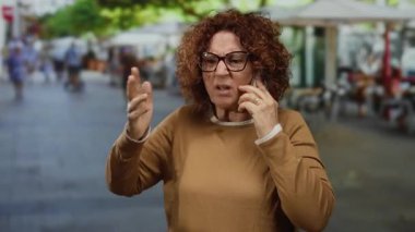 Şehirli sokak ortamında telefonla konuşurken duygusal hareketler yapan bir kadın, hayal kırıklığını ya da sohbete olan bağlılığını gösteriyor.