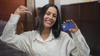 İnşaat alanında gülümseyen ve elinde mavi bir kredi kartıyla kendini gösteren bir kadın profesyonel bir çevrede kendine güven ve başarı örneği gösteriyor..