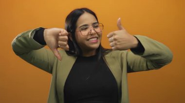 Karmaşık duyguları olan bir kadın, portakal rengi arka planda gözlük ve ceket takıyor duygularının ve kararlarının karşıtlığını gösteriyor..